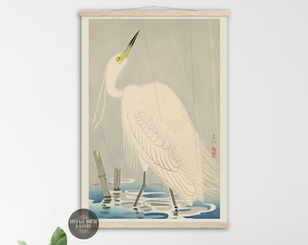 Könnte beinhalten: Ein gerahmter Druck eines weißen Reiher in einer regnerischen Szene, inspiriert von japanischer Kunst. Der Vogel steht im Wasser mit Bambusstängeln, sein Kopf ist nach oben geneigt. Das Kunstwerk zeigt eine gedämpfte Farbpalette aus Blau-, Grau- und Weißtönen.