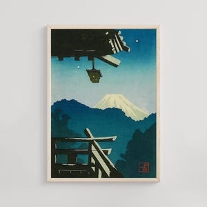 Puede incluir: Lámina artística enmarcada que representa un paisaje japonés. La impresión muestra una montaña con la cima nevada, un edificio tradicional y una linterna colgando del tejado. La paleta de colores incluye tonos de azul, verde y blanco.