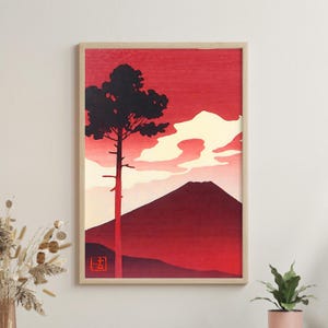 Puede incluir: Lámina artística enmarcada que representa un paisaje estilizado en tonos rojos y negros. Un árbol alto y oscuro se alza frente a una montaña y nubes. La obra de arte tiene una estética minimalista, con un cielo rojo y un pequeño cuadrado rojo con caracteres japoneses.