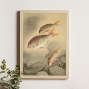 Puede incluir: Una impresión enmarcada con una ilustración de inspiración asiática de tres peces nadando. Los peces tienen aletas rojas y naranjas, sobre un fondo apagado de rocas grises y un cielo amarillo claro. El marco es de color madera clara.