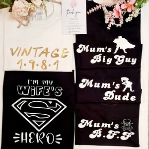 May include: Five black t-shirts with white text and graphics. The shirts feature the text "Mum's Big Guy", "Mum's Dude", "Mum's B.F.F", "I'm My Wife's Hero", and "Vintage 1.9.8.1".