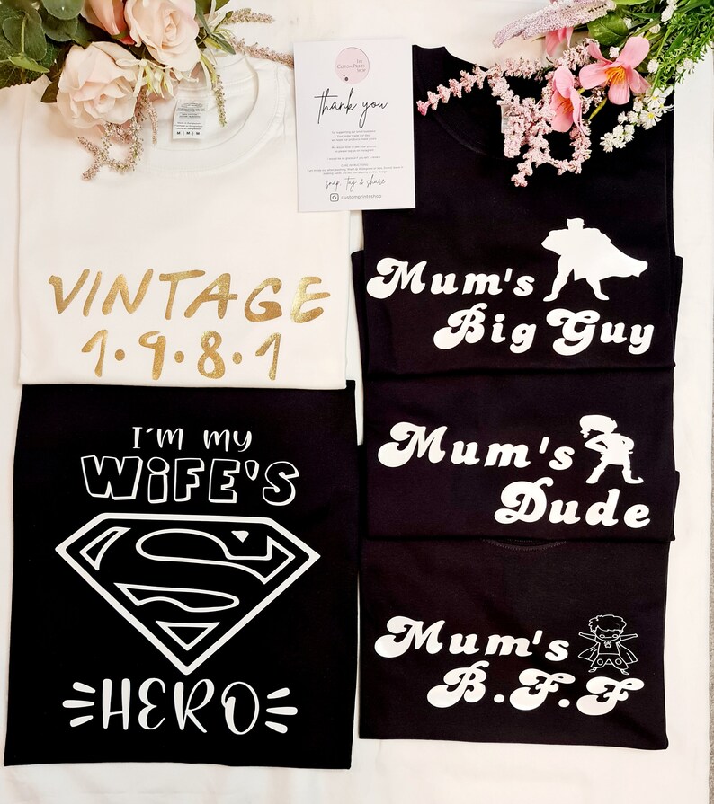 May include: Five black t-shirts with white text and graphics. The shirts feature the text "Mum's Big Guy", "Mum's Dude", "Mum's B.F.F", "I'm My Wife's Hero", and "Vintage 1.9.8.1".