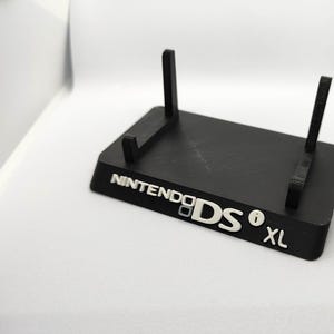 May include: A black plastic stand for a Nintendo DS XL. The stand has two vertical supports and the words "NINTENDO DS XL" are printed on the base.