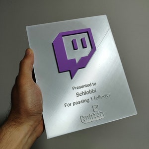 Pode incluir: Uma placa prateada com um logotipo roxo do Twitch e o texto "Apresentado a Schlobbi Por passar 1 seguidor twitch"