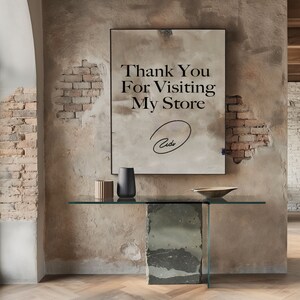 May include: A framed sign with the text "Thank You For Visiting My Store" and a handwritten signature. The sign is hanging on a wall with exposed brick. A glass-top table with a stone base sits in front of the sign.
