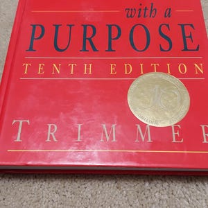 May include: A red hardcover book titled "Writing with a Purpose, Tenth Edition" by  Trimmer. The book cover features a gold seal with the words "Writing with a Purpose" and a stylized letter "J".