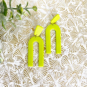 May include: A pair of lime green statement earrings with an arch shape. The earrings are made of polymer clay and have a matte finish.
