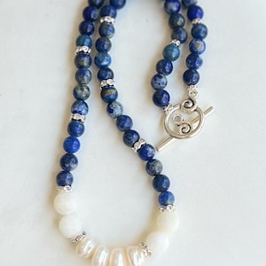 May include: A blue and white beaded necklace with a silver toggle clasp. The necklace features blue lapis lazuli beads with silver accents and white freshwater pearls.