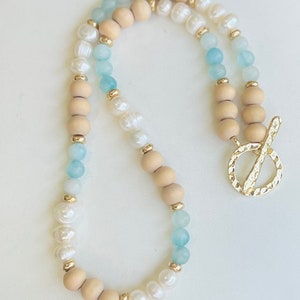 May include: A layered necklace with wooden, white pearl, and light blue beads. The necklace has a gold clasp.