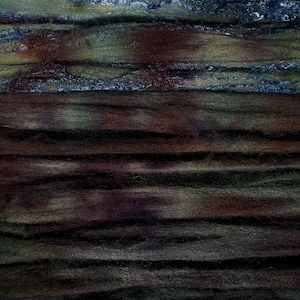 Könnte beinhalten: Abstrakte Textilkunst mit horizontalen Farbstreifen. Das Werk zeigt Schichten aus Dunkelgrün, Braun und Blautönen, wodurch ein strukturiertes, organisches Aussehen entsteht. Die verschiedenen Farbtöne und Texturen deuten auf ein natürliches, erdiges Thema hin.