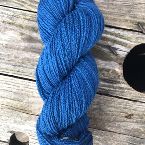 May include: A skein of bright blue yarn, tightly wound and textured. The yarn is a rich, solid colour, and appears soft. The background is a weathered wooden surface, providing a rustic contrast to the yarn's colour.