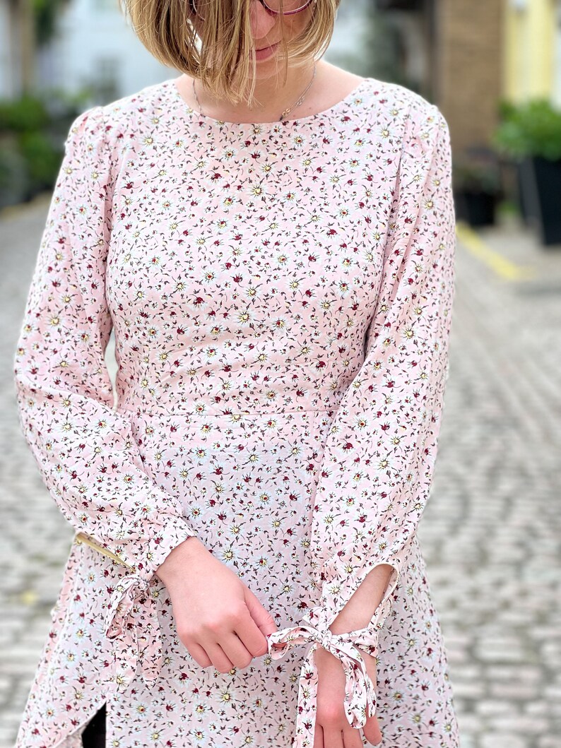 Puede incluir: Un vestido rosa de manga larga con estampado floral. El vestido tiene un escote redondo y pu&ntilde;os con cordones.