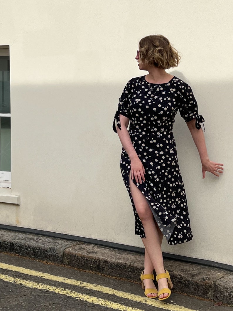 Puede incluir: Una mujer con un vestido midi negro con estampado floral blanco y sandalias de tac&oacute;n amarillo. El vestido tiene una abertura lateral y las mangas est&aacute;n atadas en las mu&ntilde;ecas.