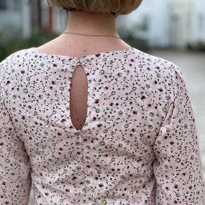 Puede incluir: Un vestido rosa floral con un escote en la espalda en forma de ojo de cerradura y una cremallera. El vestido tiene un peque&ntilde;o estampado floral con flores blancas y hojas verdes sobre un fondo rosa.