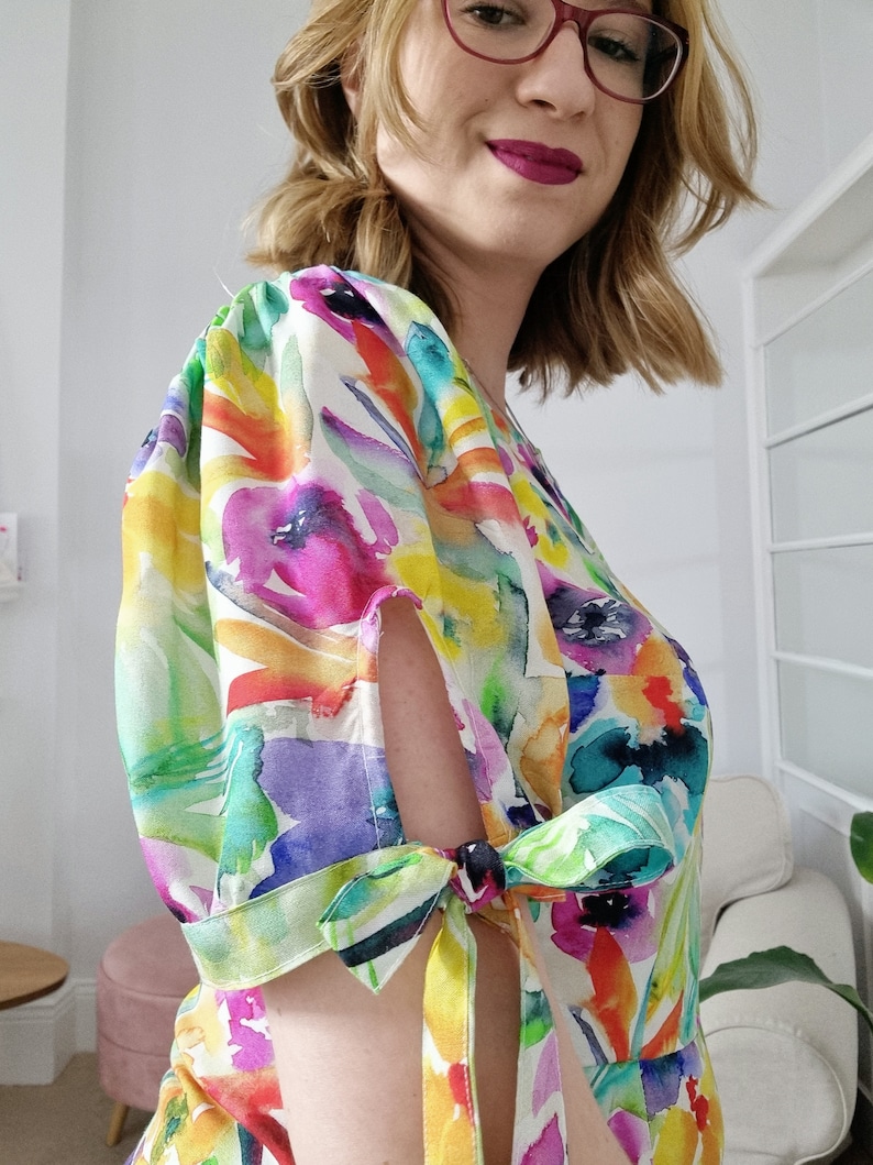 Puede incluir: Un vestido blanco con estampado floral colorido y mangas abullonadas. Las mangas tienen un detalle de lazo en la mu&ntilde;eca.