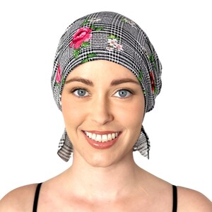 May include: A black and white patterned headscarf with pink and red roses and green leaves. The headscarf is tied in a knot at the back of the head.