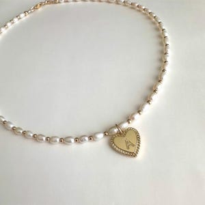 May include: A delicate pearl necklace with a gold heart charm featuring the letter 'A'.