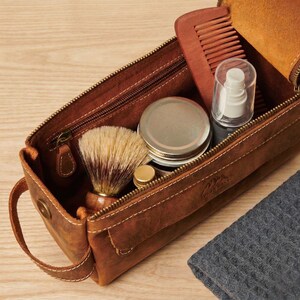 Wide-mouth leather travel bag open on a light wooden surface showing spacious interior capacity.