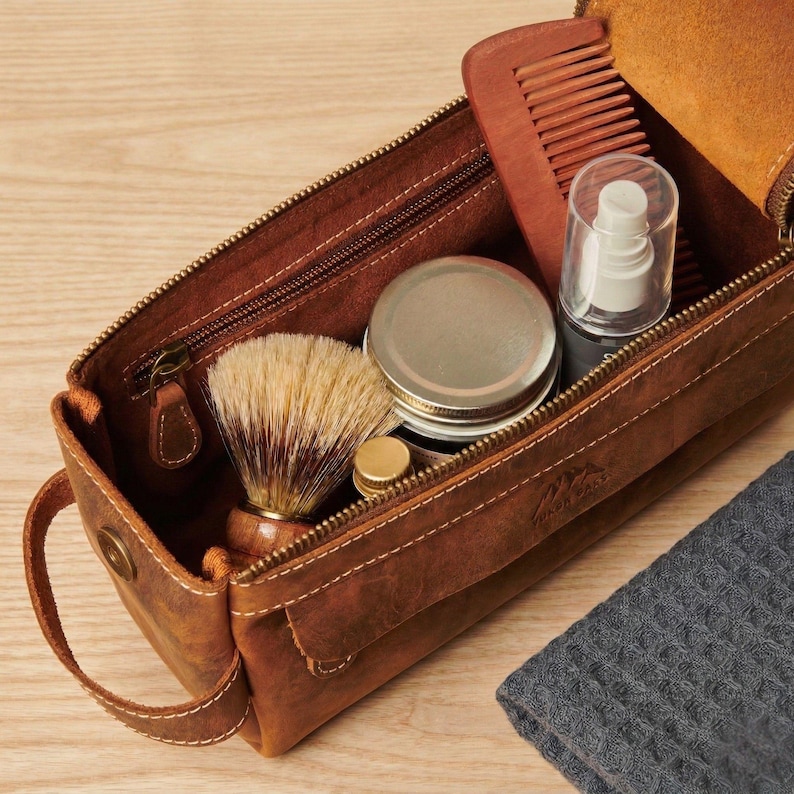 Wide-mouth leather travel bag open on a light wooden surface showing spacious interior capacity.