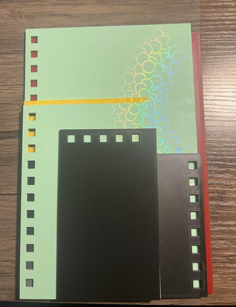 Puede incluir: Un surtido de hojas de papel de colores, incluyendo verde, negro y rojo, con bordes perforados para encuadernar. La hoja verde tiene un patr&oacute;n hologr&aacute;fico iridiscente. Las hojas est&aacute;n dispuestas sobre una superficie de madera.