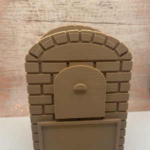 May include: A brown 3D printed model of a brick oven with a small door and a rectangular opening below. The oven is made to look like a traditional brick oven with a rounded arch.