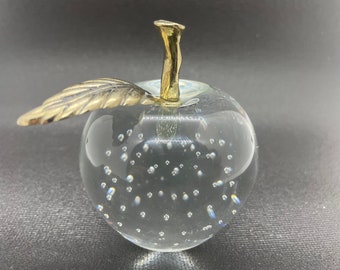 Könnte beinhalten: Ein durchsichtiger Glasapfel-Briefbeschwerer mit einem goldenen Stiel und Blatt. Der Apfel ist mit kleinen Luftblasen gefüllt.