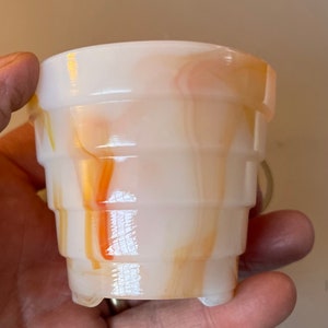 May include: A white and orange marbled glass planter with a fluted design. The planter has a rounded base and a wide opening.