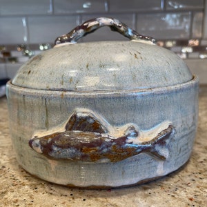 May include: A ceramic lidded dish with a blue glaze and a brown fish design. The dish has a handle on the lid.