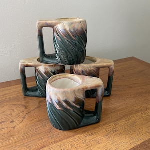 May include: A set of four ceramic mugs featuring a distinctive twisted, spiral-textured body. Each mug displays a gradient glaze transitioning from a deep, dark forest green at the base to a warm, creamy beige and brown tone at the top rim.
