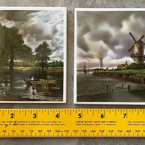 May include: Two square ceramic tiles with landscape paintings. One depicts a river scene with a horse-drawn cart, the other a windmill by a waterway. The tiles are approximately 4 inches square.