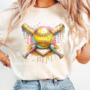 May include: A white t-shirt with a graphic design of a yellow softball with pink and blue dripping paint, crossed baseball bats, and a white home plate.