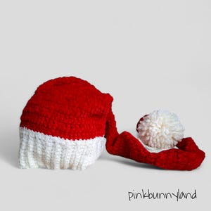 May include: A red and white crocheted Santa hat with a white pom-pom on the end of the hat's tail.