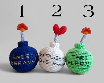 May include: Three crocheted bomb-shaped ornaments. The blue bomb says "Sweet Dreams", the white bomb says "Explosive Love Inside", and the green bomb says "Fart Alert!". Each has a different topper.