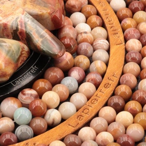 Peut inclure: Gros plan sur un cercle en bois avec les mots "Lapierre" et "Lapierreff" imprimés dessus. Le cercle est entouré d'une chaîne de petites pierres rondes roses, brunes et blanches.