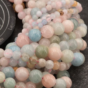 May include: A close-up of a strand of round, smooth beads in shades of pink, blue, and green. The beads are made of aquamarine and are strung together with a thin, clear thread.