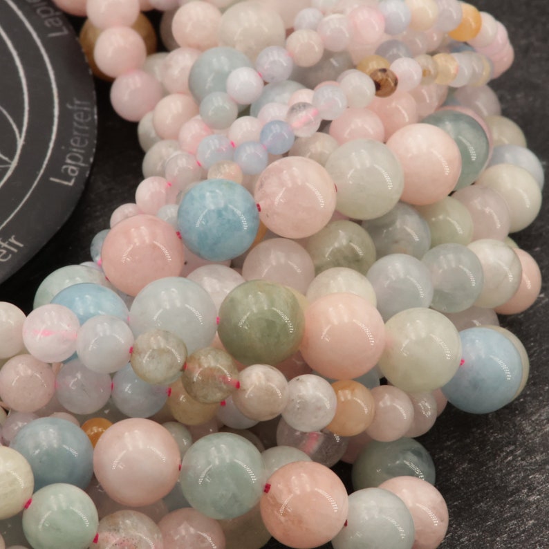 May include: A close-up of a strand of round, smooth beads in shades of pink, blue, and green. The beads are made of aquamarine and are strung together with a thin, clear thread.
