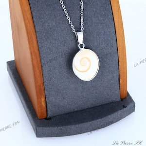 Peut inclure: Un collier en chaîne argent avec un pendentif rond orné d'un coquillage blanc et orange. Le pendentif est serti dans une bélière en argent.