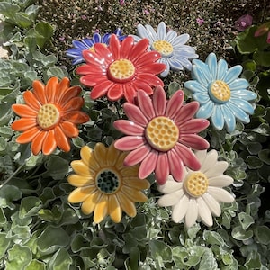 Peut inclure: Assortiment de piquets de jardin en céramique en forme de fleurs de différentes couleurs, dont le rouge, le rose, le jaune, le bleu et l'orange. Les fleurs ont une forme de marguerite avec plusieurs pétales.