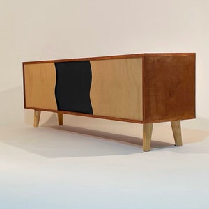 May include: A wooden cabinet with two sliding doors. The doors are made of plywood and have a black and natural wood design. The cabinet is sitting on four wooden legs.