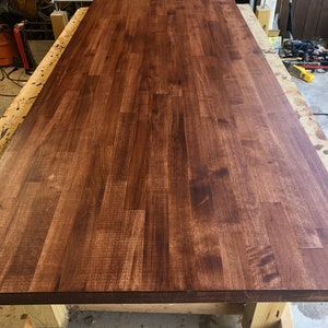 May include: A close-up of a large, dark brown wooden countertop. The countertop is made of multiple pieces of wood that have been joined together to create a seamless surface. The wood has a natural grain pattern and a smooth finish.