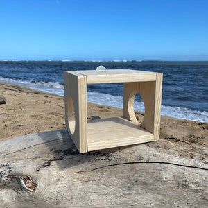May include: A wooden birdhouse with two circular openings, sitting on a weathered log against a blue sky and ocean background.