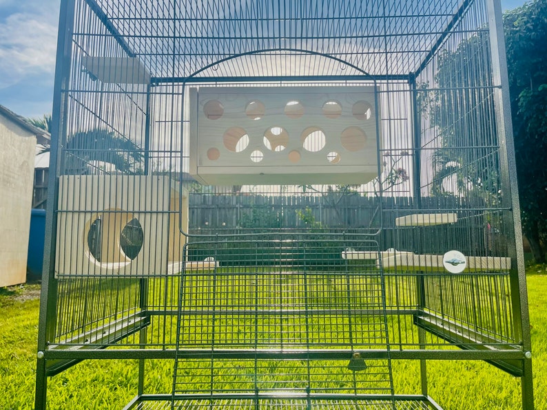 May include: A large black metal cage with multiple wooden platforms and a white wooden perch. The cage is designed for small animals like birds or rodents.