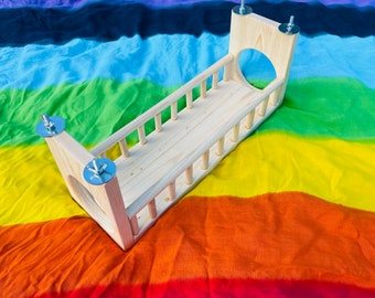 Puede incluir: Una cama de columpio de madera con un diseño de listones y herrajes metálicos. La cama de columpio está colgada de un fondo de tela de colores.