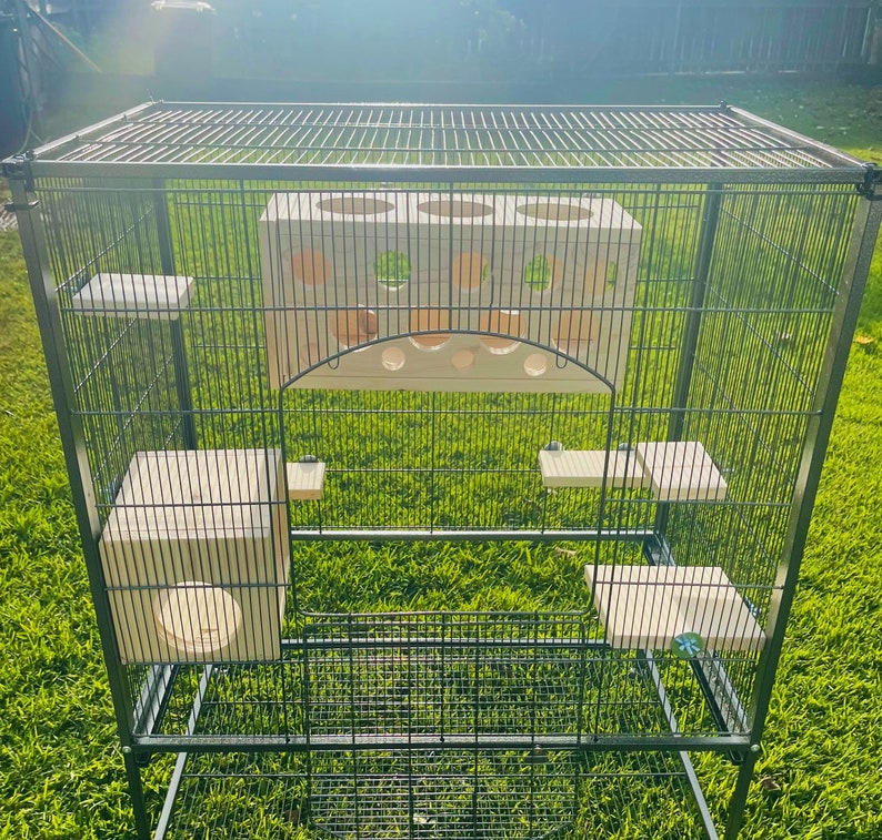 May include: A black metal cage with multiple levels and a white wooden play structure inside. The cage has a wire mesh design and is suitable for small animals.
