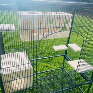 May include: A black metal cage with multiple wooden platforms and a wooden toy with holes for a pet. The cage is on a green grassy surface.