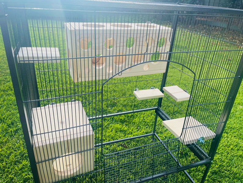 May include: A black metal cage with multiple wooden platforms and a wooden toy with holes for a pet. The cage is on a green grassy surface.