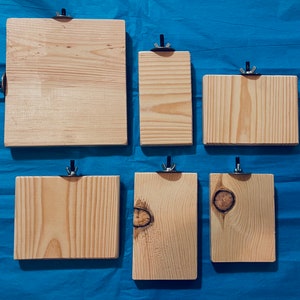 Puede incluir: Seis letreros de madera con herrajes de metal para colgar. Los letreros son de diferentes tamaños y están hechos de madera natural de color marrón claro.