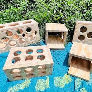May include: Four wooden boxes with different sized circular openings. The boxes are made of light wood and are arranged on a blue and green patterned fabric.