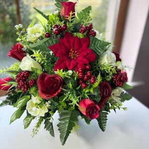 May include: A colourful floral arrangement with deep red poinsettias, roses, and berries, complemented by white flowers and green foliage. The bouquet is carefully arranged, creating a visually appealing display. This decorative piece is suitable for various occasions.