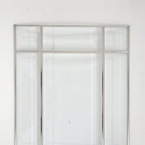 May include: A rectangular mirror with a silver metal frame and clear glass panels. The mirror is divided into sections, with a large central panel and smaller panels around the edges. The design is geometric and modern.